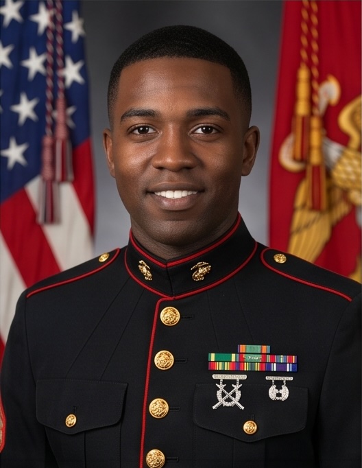 Staff Sergeant Marcus Ellis in U.S. Marine Corps dress uniform with American and Marine Corps flags behind him.